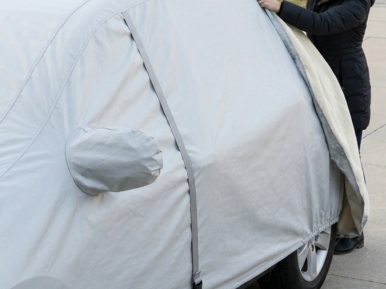 A woman in a winter coat pulling the cover down over the rear window of a mid-size SUV